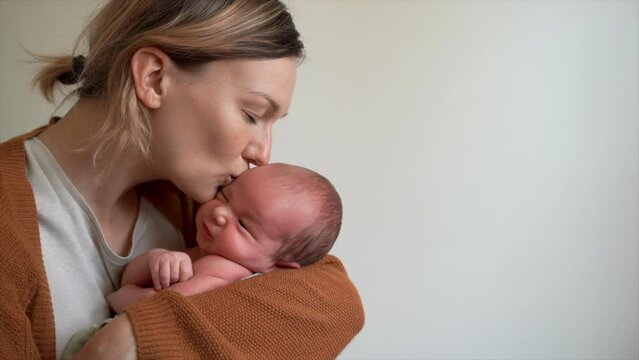 Mother and baby. Loving mom holding newborn son in arms and kissing on head. Healthy physical and mental development of child, happy maternity and family.