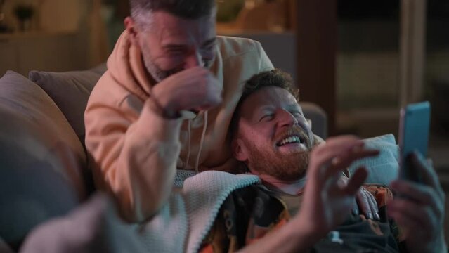 Happy Male Gay Couple Relaxing On Couch With Smartphone