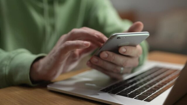 Close up man using smartphone at laptop