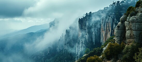 Cloudy and foggy weather surrounds cliffs with trees near Montserrat Abbey in Spain.