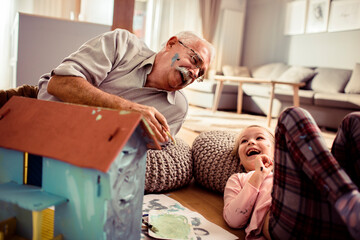 Grandfather painting small toy house with granddaughter at home