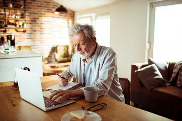Senior man working at home with laptop and papers on desk