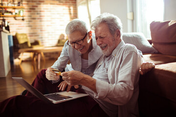 Happy senior couple using credit card on laptop at home