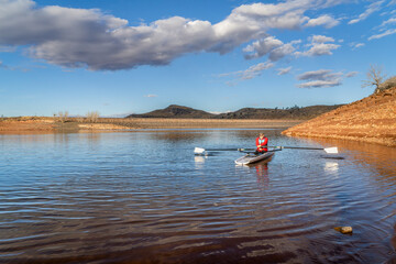 Senior male rower is rowing a coastal rowing shell - Horsetooth Reservoir in fall or winter scenery...