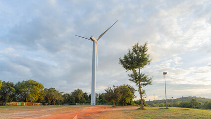 Picture of a large white wind turbine for generating electricity, located in the middle of a large plaza on the top of the mountain. with trees growing around