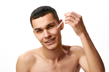 Young handsome man taking care after skin, applying moisturizing face serum against white studio background. Concept of male beauty, skin care, spa, cosmetology, men's health