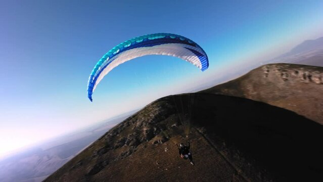 Aerial view from a sports FPV drone. A paraglider athlete flies near the slopes of a small mountain. Free paragliding flight over rural fields in autumn Video from FPV drone