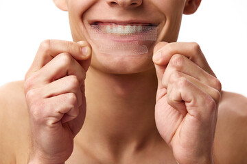 Cropped image of male face against white studio background. Man whitening teeth with whitening strips. Concept of male beauty, dental care, spa, cosmetology, men's health