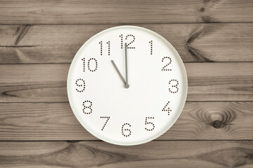 Eleven o'clock. Time management or business concept. Plain white wall clock showing 11 am on a wooden background. Copy space. Opening or closing hours. Schedule or working, study hours.