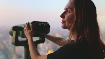 Woman enjoy Bangkok cityscape on Baiyoke Tower Sky viewpoint. Girl looking in binoculars telescope...