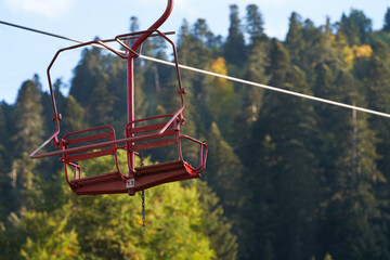Two-seat cable car chair number 13 in the air on a cable against a backdrop of forested mountains.