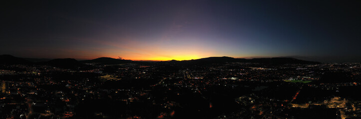 Fototapeta premium Dusk panorama at a city with night lights and the sky with colors and the sun going down the mountains. Almost night.