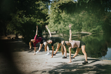 Fit girls enjoying outdoor sports and stretching exercises in a city park on a sunny day. Friends...