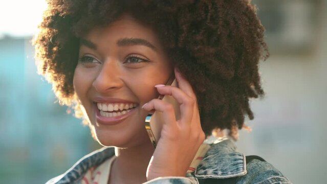 Laughing curly haired African woman talking on cellphone outdoors