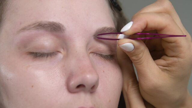 makeup artist plucks a young woman's eyebrows with tweezers. Beautiful thick eyebrows close-up. Professional makeup and cosmetological skin care in a beauty salon