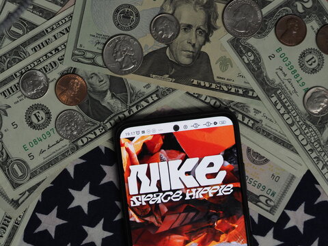 In this photo illustration, a Space Hippie logo seen displayed on a smartphone with United States Dollar notes and coins in the background. Space Hippie  brand owned by Nike, Inc. corporation