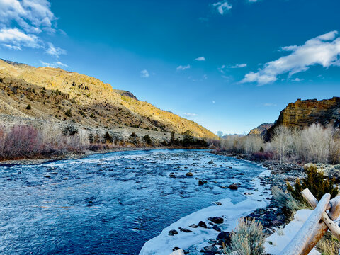 Shoshone River with snow melt in December is flowing near Cody, Wyoming, and the Northfork Highway. High cliffs are set off with yellow sunlight and deep blue sky