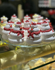 New Year's dessert, meringues in the form of snowmen with red hats and scarves, stand on a platter, in a store. Increase in price of desserts, consumption of sweets during the holidays