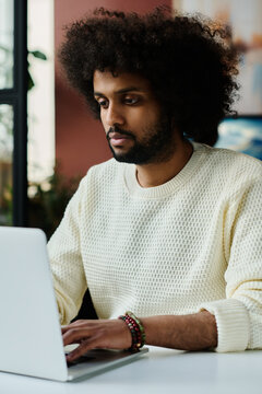 Young serious man typing on laptop keyboard and looking at screen with online information while organizing work or carrying out task