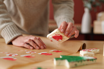 Fototapeta na wymiar Hands of young unrecognizable woman making prints of Santa cap while holding workpiece over unrolled piece of craft paper