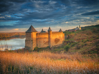 Golden light of sun on grass and walls on fortress under sky with clouds - obrazy, fototapety, plakaty