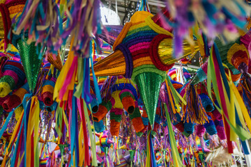 Colorful piñatas of different shapes and sizes hanging over the stalls of a traditional Mexican...