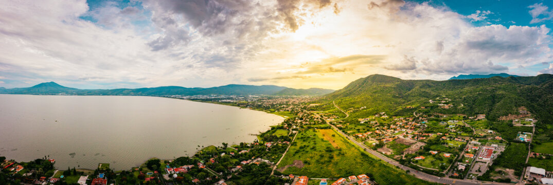 A panorama of mountains and lake with the sunset as background. Clouds and blue sky with trees and colors
