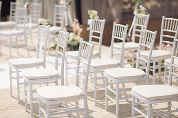 Ceremony in the bosom of nature. White chairs with flowers set in the grass. white chairs lined up for an event accompanied by a bouquet of white flowers.