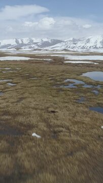 Fast Flying over Small Lakes with Ice Blocks in Spring. Snowy Mountains on Background. Aerial Low Angle View. Arabel Plateu. Kyrgyzstan. Vertical Video