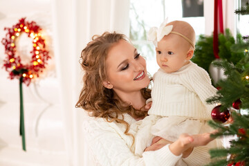 Obraz na płótnie Canvas close-up portrait of a beautiful mother showing an elegant Christmas tree to her little daughter. mother with a child in her arms against the backdrop of a Christmas tree decorated for Christmas