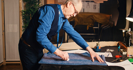 Senior couturier fabricating material to design custom made fashion items, needlework concept. Small buisness owner manufacturing clothes with professional fabric in tailor workshop.