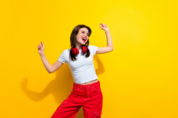 Portrait of pleasant pretty girl wear white t-shirt dancing in headphones look at promo empty space isolated on yellow color background