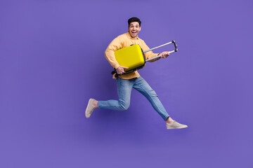 Full body photo of nice young male running hold suitcase traveler dressed stylish yellow outfit isolated on purple color background