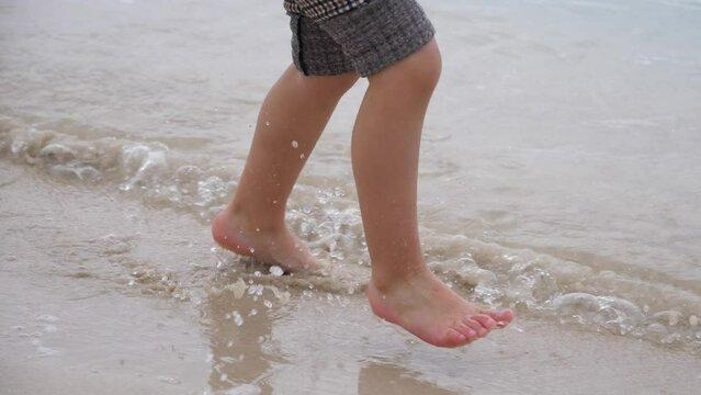 Little barefoot legs of child girl running playfully on shallow water edge Malta Mediterranean sea beach