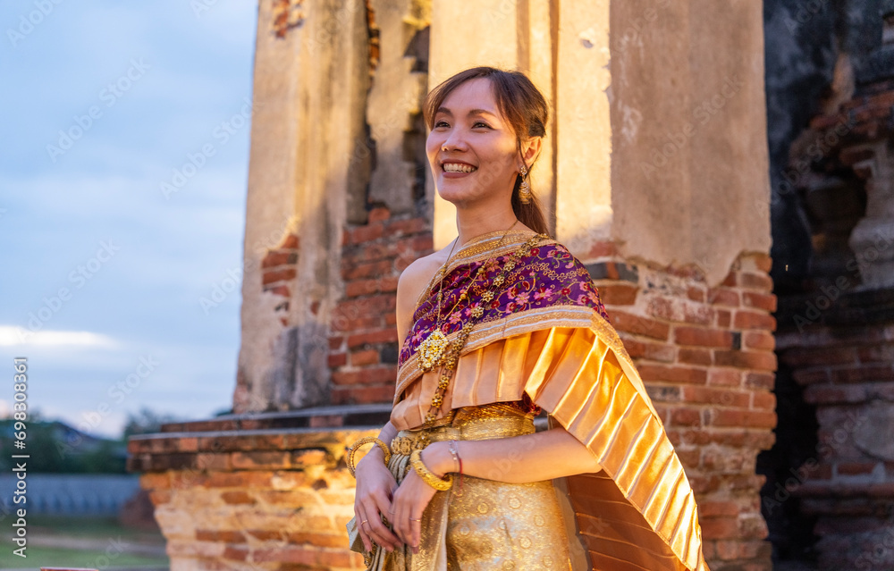 Wall mural tourist asian woman wearing thai national costume, smiling brightly, standing at an old church, tour