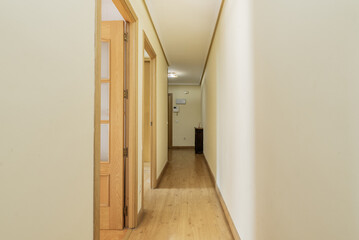 A long hallway in a house with light wooden floors and doors