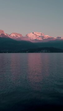 Drone vertical footage of Annecy lake with snow-peaked mountains in the background at sunset, France