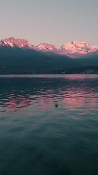 Vertical drone footage of a person standing on the shore of Annecy lake at sunset in Duingt, France
