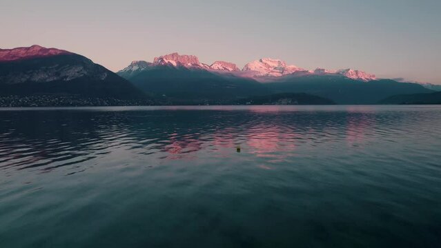 Drone footage of a person standing on the shore of Annecy lake spreading his arms at sunset, France