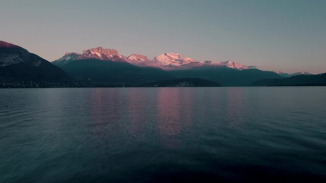 Drone shot of Annecy lake with snow-peaked mountains in the background at sunset in Duingt, France