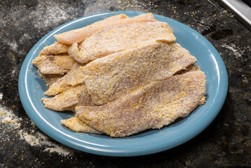 A plate of fish fillet encrusted with a mix of wheat and corn flour mix ready for pan frying. Home...