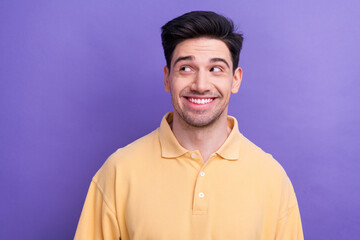 Photo of confident dreamy man dressed yellow shirt smiling looking empty space isolated purple color background