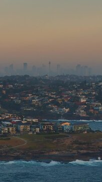 Vertical drone footage of the cityscape of Sydney as seen from Maroubra Beach at sunset, Australia