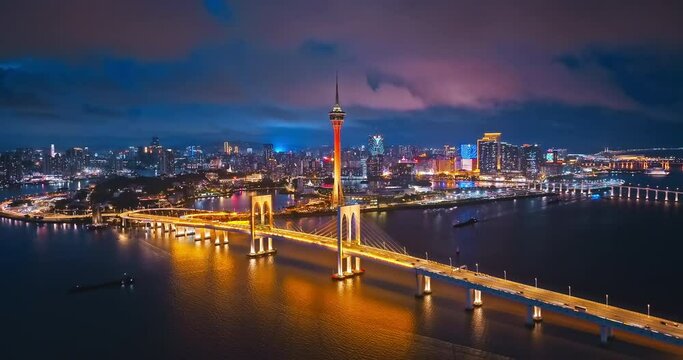 Aerial footage of Macau city skyline with modern buildings scenery at night. River and bridge with city buildings scene. Drone surround shooting.