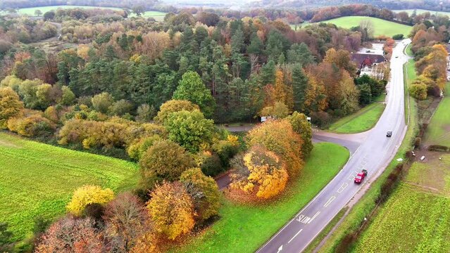 Drone shot of cars driving on an intercity road with colorful autumn trees in Oxted, Surrey, England
