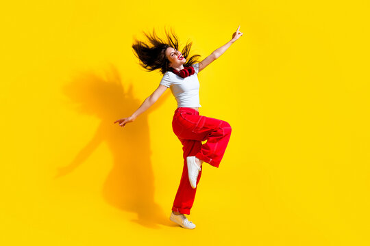 Full length photo of sweet dreamy woman dressed t-shirt headphones flying hair arms sides having fun discotheque isolated yellow color background