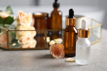 Bottles of cosmetic serum and beautiful flower on gray table, closeup