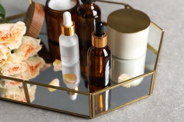Fototapeta na wymiar Bottles of cosmetic serum, beauty products and flowers on gray table, closeup