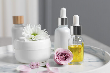 Obraz na płótnie Canvas Bottles of cosmetic serum, cream jar and flowers on table, closeup