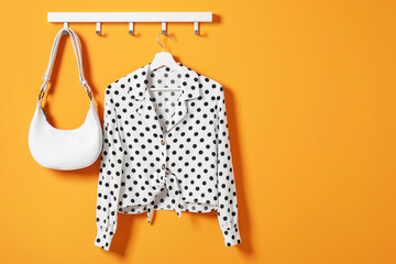 Hanger with polka dot shirt and bag on orange wall, space for text - obrazy, fototapety, plakaty